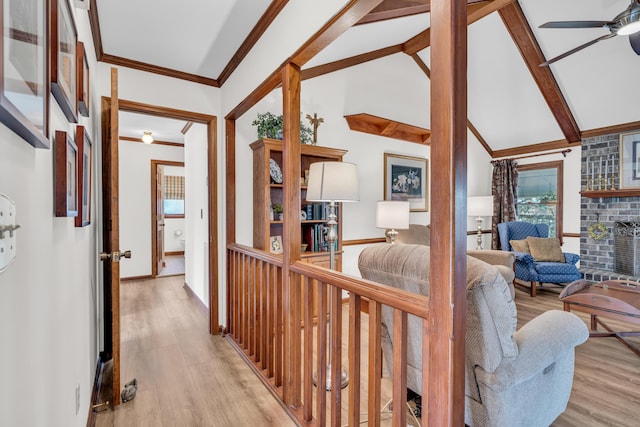 interior space with a fireplace, light wood-style flooring, lofted ceiling with beams, ornamental molding, and a ceiling fan