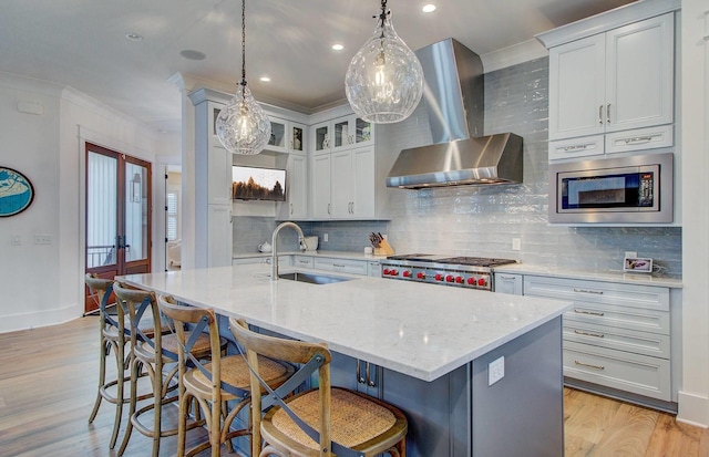 kitchen with stainless steel microwave, sink, light hardwood / wood-style flooring, decorative backsplash, and wall chimney exhaust hood