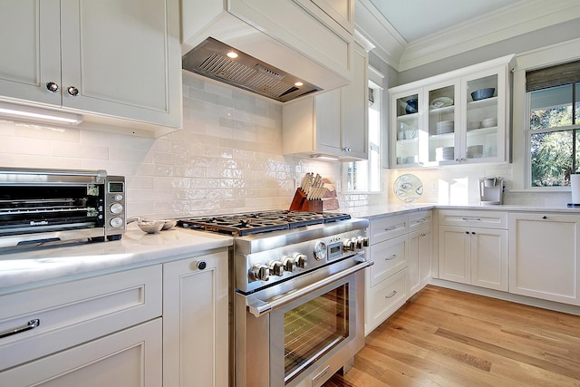 kitchen featuring light wood-type flooring, stainless steel range, backsplash, white cabinets, and custom range hood