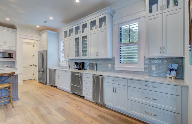 kitchen with decorative backsplash, light hardwood / wood-style flooring, white cabinetry, light stone countertops, and stainless steel appliances