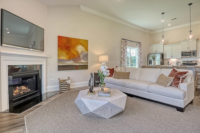 living room featuring wood finished floors, ornamental molding, a glass covered fireplace, and baseboards