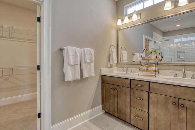 full bathroom featuring tiled shower, double vanity, a walk in closet, tile patterned floors, and baseboards
