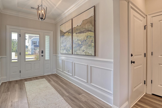 entryway featuring wood finished floors, a chandelier, ornamental molding, a wainscoted wall, and a decorative wall