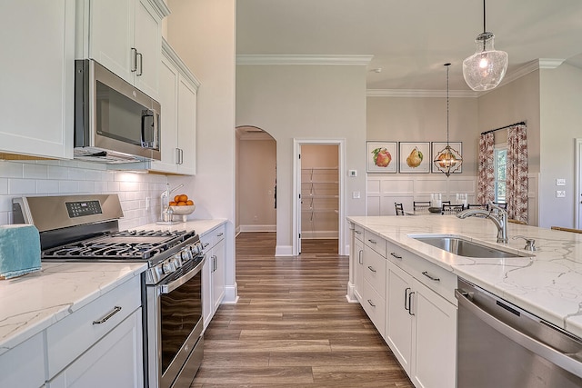 kitchen with stainless steel appliances, a sink, crown molding, arched walkways, and wood finished floors