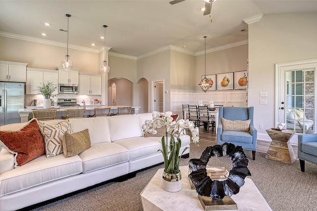 living room featuring arched walkways, a high ceiling, a ceiling fan, crown molding, and carpet floors