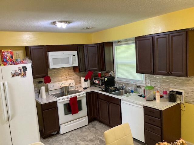 kitchen with a textured ceiling, white appliances, dark brown cabinetry, and sink