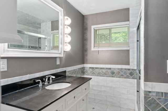 bathroom featuring a shower with door, vanity, and tile walls