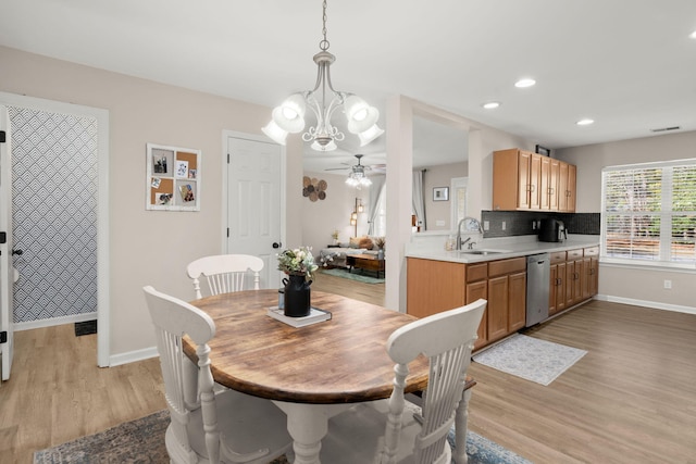 dining room with ceiling fan with notable chandelier, sink, and light hardwood / wood-style flooring