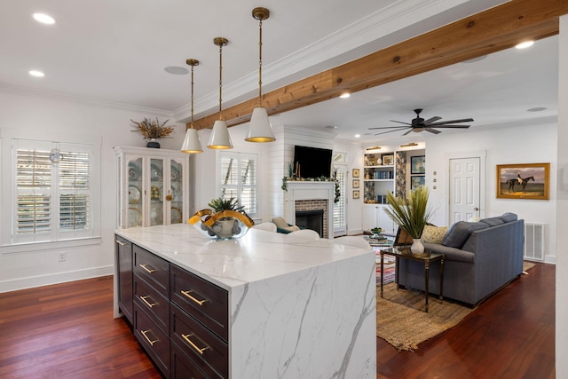 kitchen with light stone countertops, dark wood-type flooring, pendant lighting, a fireplace, and a kitchen island