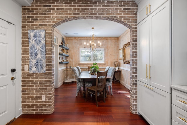 dining space featuring a notable chandelier, dark hardwood / wood-style floors, and brick wall