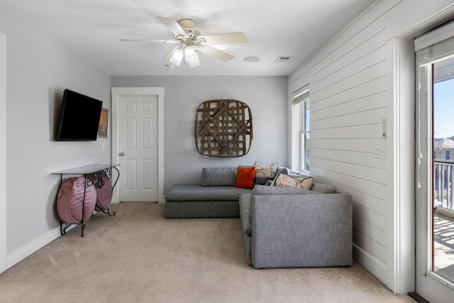 carpeted living room featuring ceiling fan, plenty of natural light, and wood walls