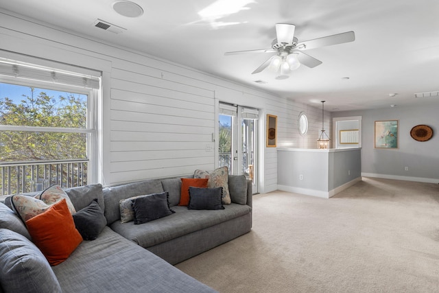 living room with ceiling fan, light colored carpet, a healthy amount of sunlight, and wood walls