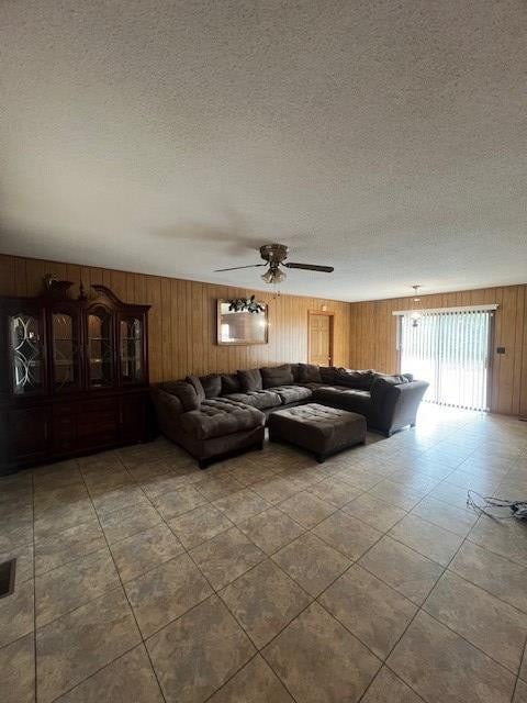 unfurnished living room featuring wooden walls, ceiling fan, and a textured ceiling