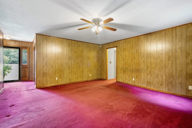 empty room featuring ceiling fan, a textured ceiling, wooden walls, and carpet flooring