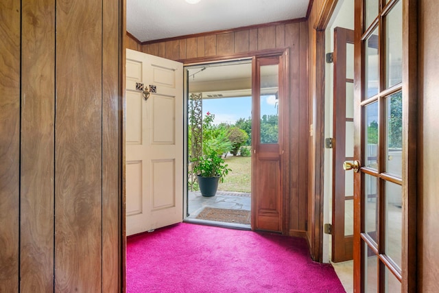 foyer entrance with light carpet, wooden walls, and crown molding