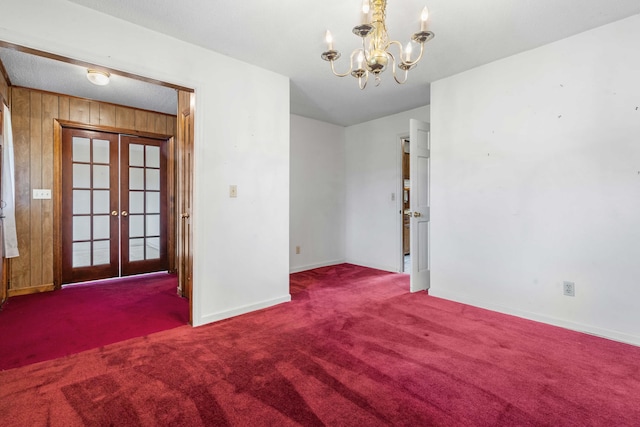 spare room with a chandelier, carpet, wood walls, and french doors