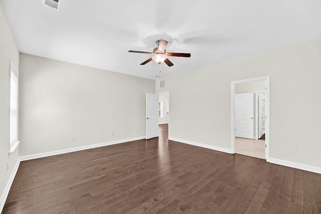 empty room featuring a ceiling fan, a healthy amount of sunlight, baseboards, and dark wood-type flooring