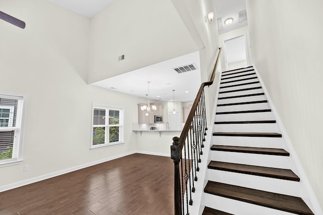 stairway featuring a towering ceiling, visible vents, wood finished floors, and baseboards