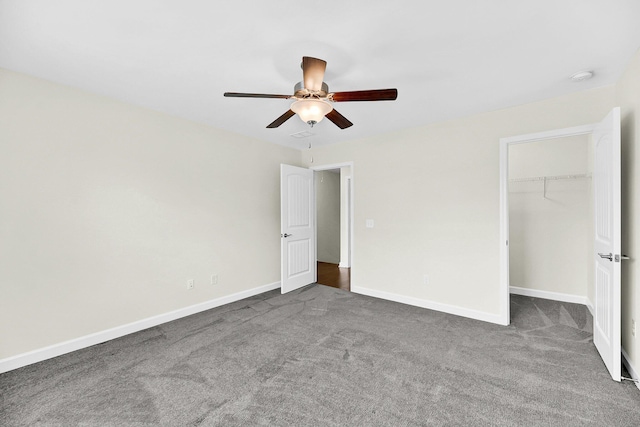 unfurnished bedroom with carpet flooring, a closet, ceiling fan, a walk in closet, and baseboards