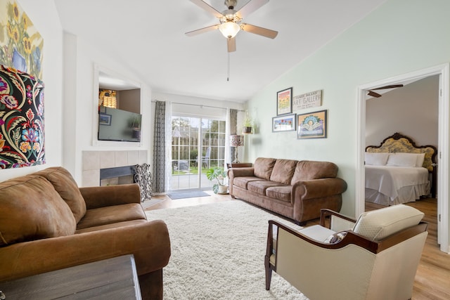 living room featuring a tiled fireplace, vaulted ceiling, ceiling fan, and light hardwood / wood-style floors