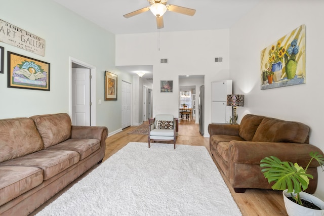 living room featuring a high ceiling, ceiling fan, and light hardwood / wood-style flooring