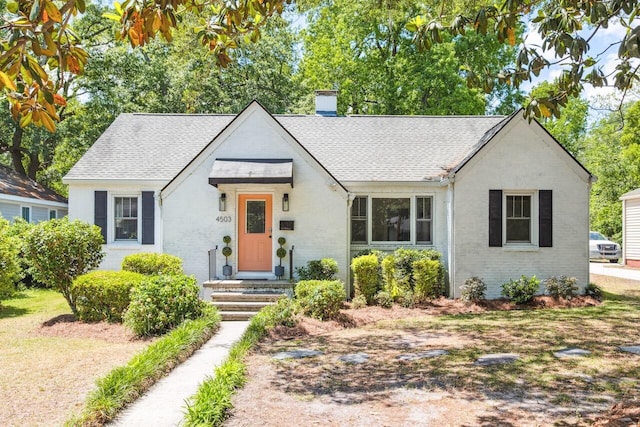 view of front of house featuring brick siding, a chimney, and roof with shingles