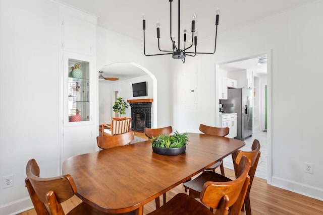 dining area with crown molding, a brick fireplace, baseboards, a notable chandelier, and light wood-style flooring