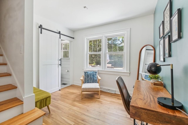 home office with visible vents, a barn door, light wood finished floors, and baseboards