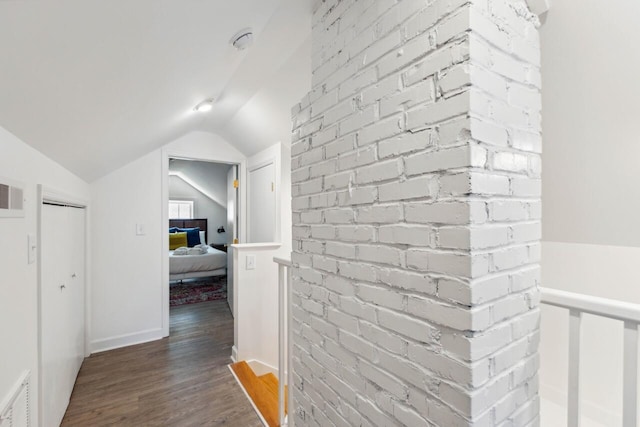 hallway with visible vents, baseboards, wood finished floors, and vaulted ceiling