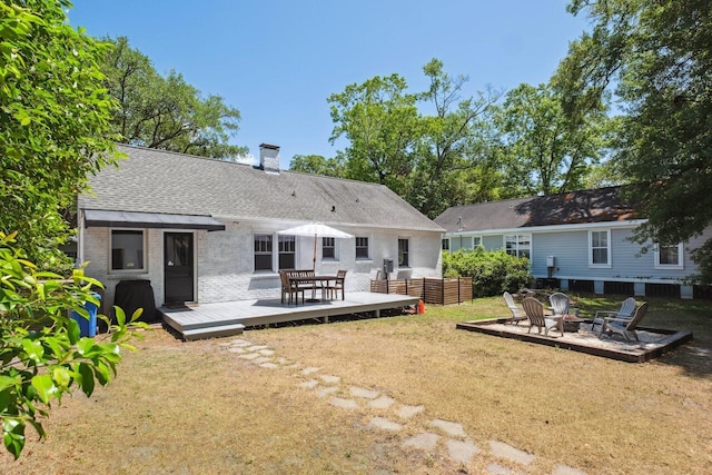 rear view of property with an outdoor fire pit, brick siding, a deck, a chimney, and a yard