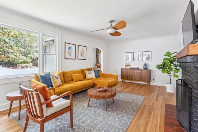 living room featuring light wood-style floors, ornamental molding, a brick fireplace, and ceiling fan