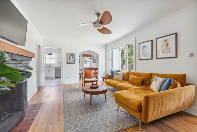 living area with crown molding, arched walkways, a ceiling fan, baseboards, and wood finished floors