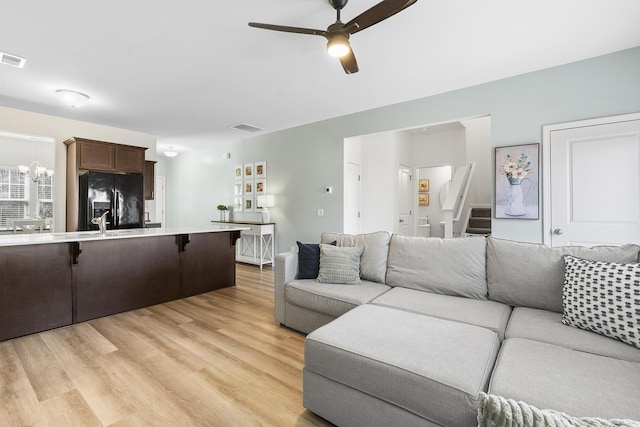 living area featuring ceiling fan with notable chandelier, light wood-style flooring, and visible vents