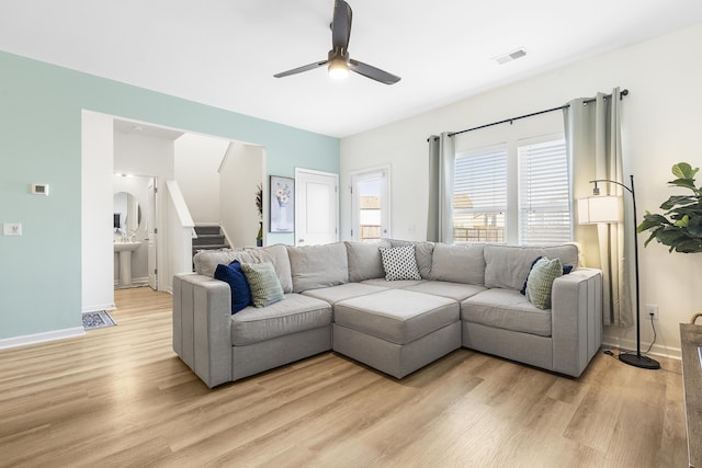 living area with light wood-style flooring, visible vents, baseboards, a ceiling fan, and stairway