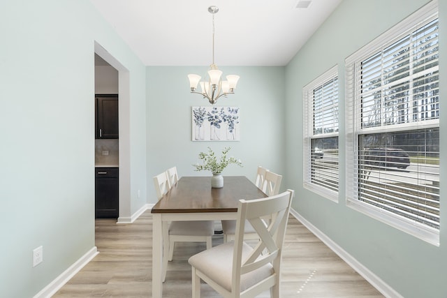 dining space with a chandelier, baseboards, and light wood finished floors