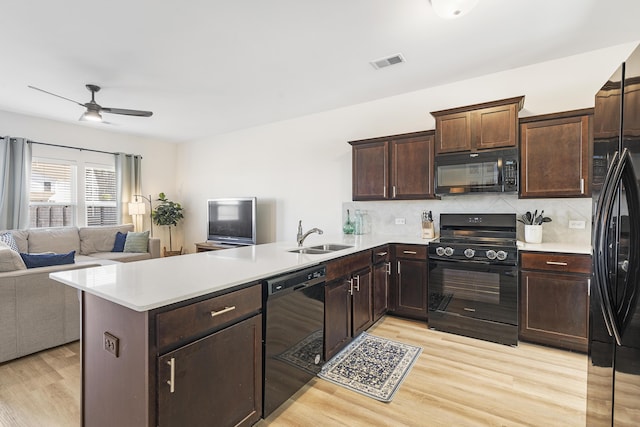 kitchen with open floor plan, a peninsula, light wood-type flooring, black appliances, and a sink