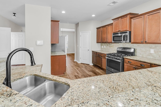 kitchen featuring visible vents, light wood finished floors, a sink, decorative backsplash, and stainless steel appliances