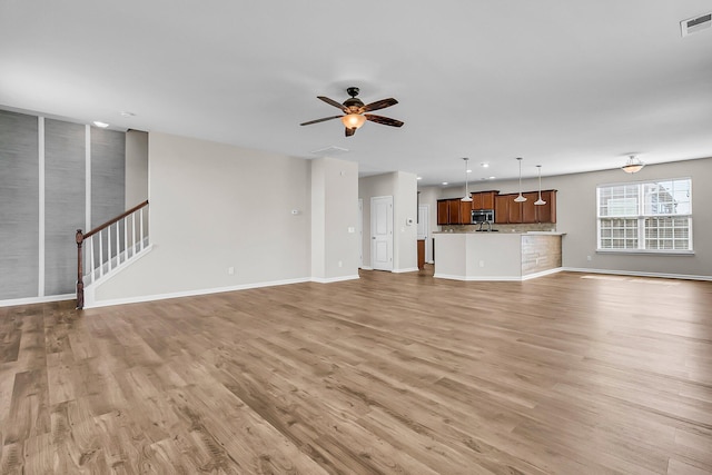 unfurnished living room featuring a ceiling fan, visible vents, baseboards, stairs, and light wood-type flooring