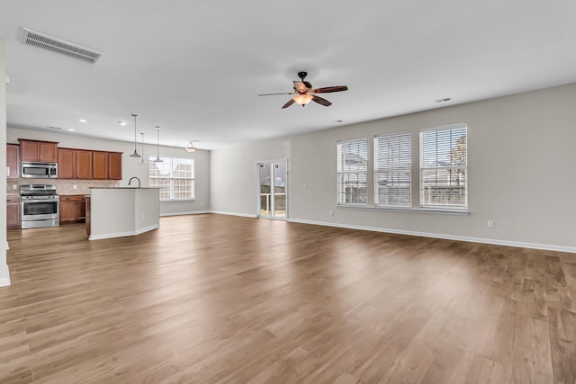 unfurnished living room featuring visible vents, baseboards, light wood-style floors, and a ceiling fan