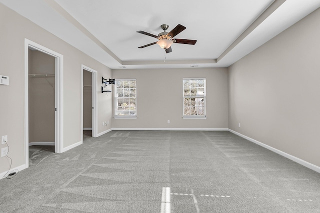 carpeted spare room featuring a ceiling fan, a raised ceiling, and baseboards