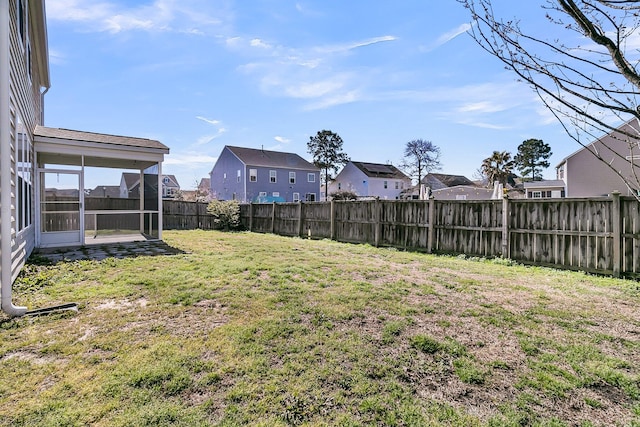 view of yard featuring a residential view, a fenced backyard, and a sunroom