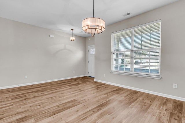 empty room with visible vents, baseboards, an inviting chandelier, and light wood finished floors