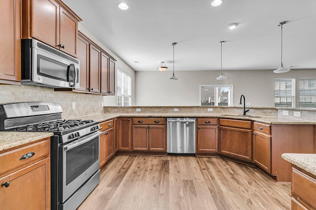 kitchen with backsplash, light wood-type flooring, brown cabinetry, stainless steel appliances, and a sink