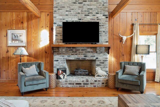 interior space with beamed ceiling, hardwood / wood-style flooring, a brick fireplace, and wooden walls