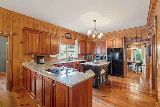 kitchen with light stone countertops, a notable chandelier, pendant lighting, light hardwood / wood-style floors, and black appliances