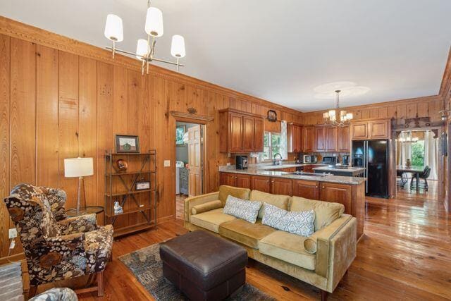 living room featuring an inviting chandelier, sink, wooden walls, ornamental molding, and wood-type flooring