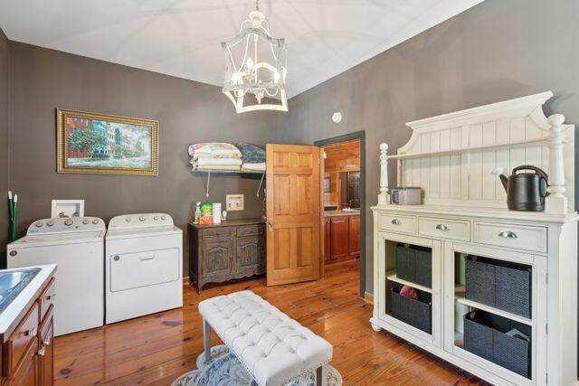 clothes washing area with washer and clothes dryer, wood-type flooring, and a chandelier