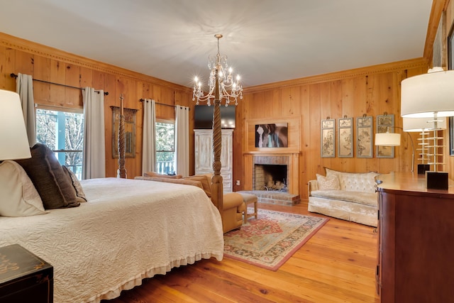 bedroom featuring an inviting chandelier, wooden walls, hardwood / wood-style flooring, ornamental molding, and a fireplace