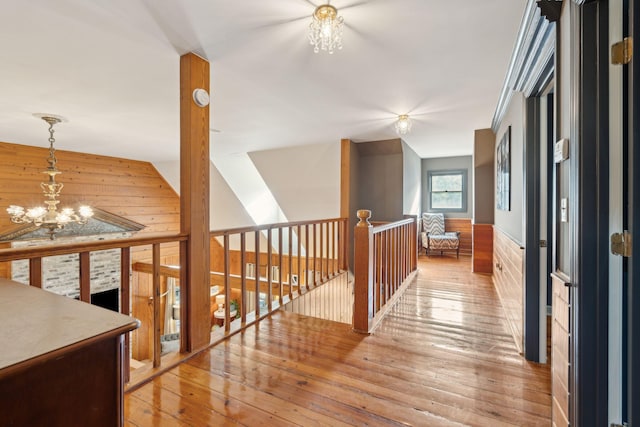 hallway featuring light hardwood / wood-style floors, wooden walls, and an inviting chandelier