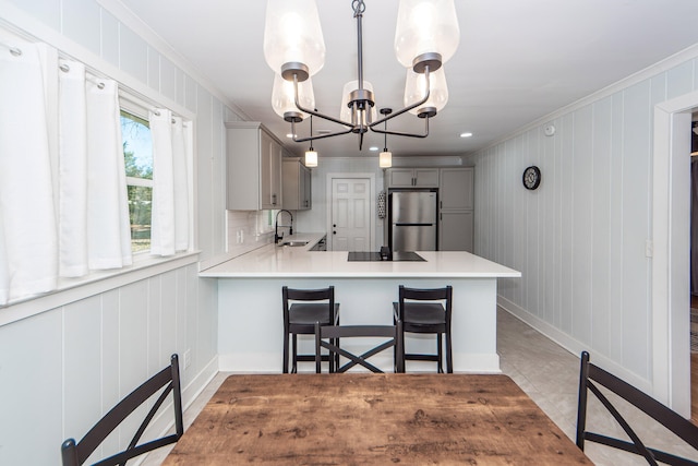 kitchen featuring hanging light fixtures, crown molding, kitchen peninsula, gray cabinets, and stainless steel fridge